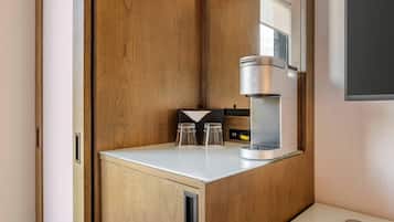 A compact kitchenette with a built-in coffee maker, two glasses, and a small cabinet.