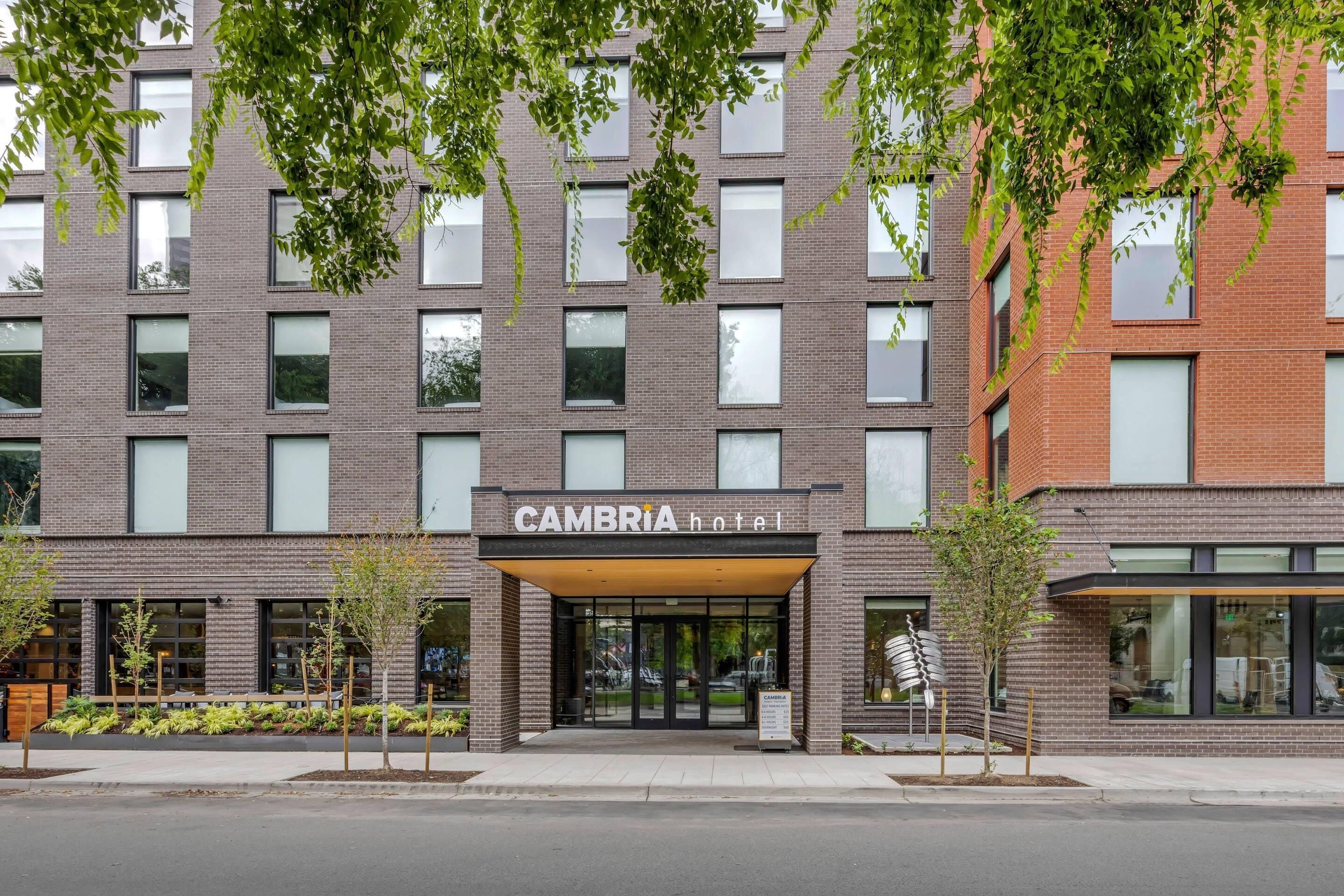 Un hôtel moderne, avec une façade en briques, de grandes fenêtres et une enseigne indiquant « CAMBRIA hotel ».