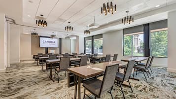 A conference room with tables, chairs, a projector screen, and large windows.