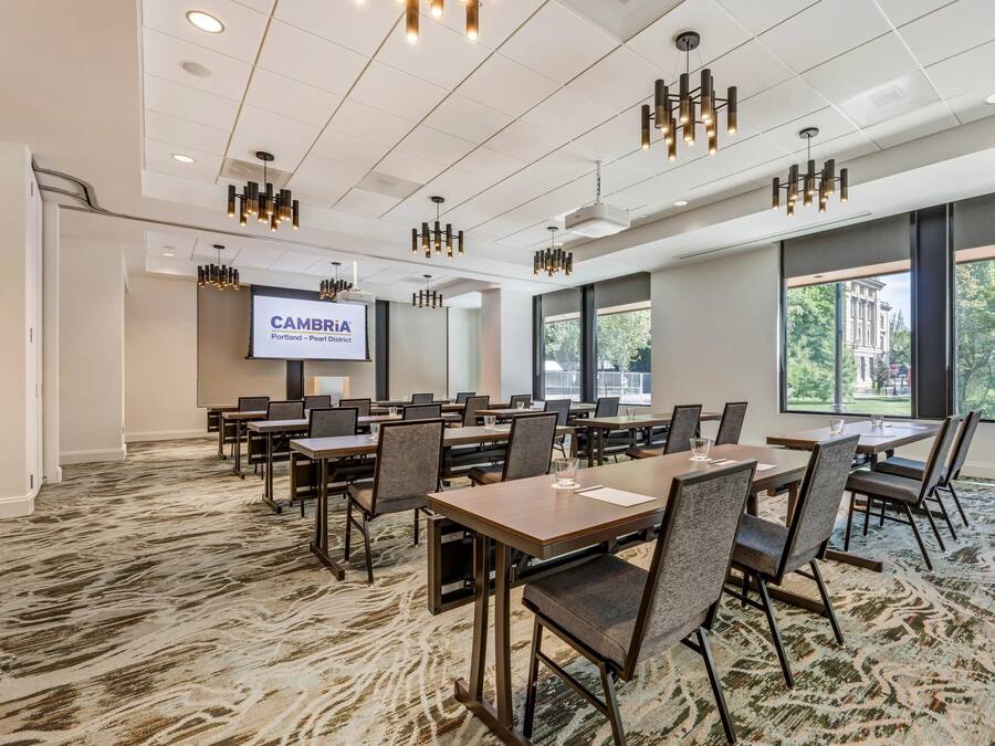 A conference room with tables, chairs, a projector screen, and large windows.