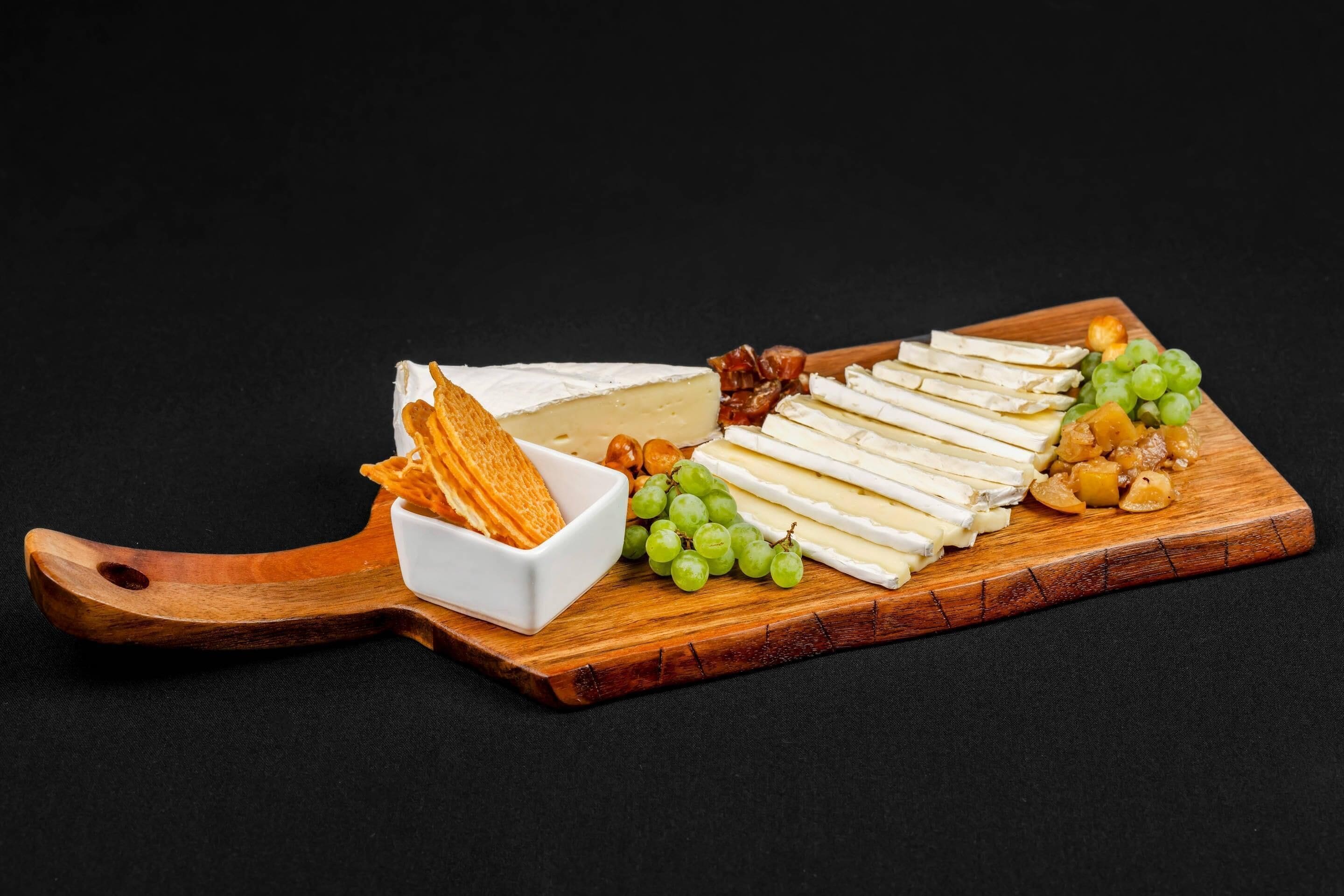 A wooden board with cheese, grapes, and crackers.