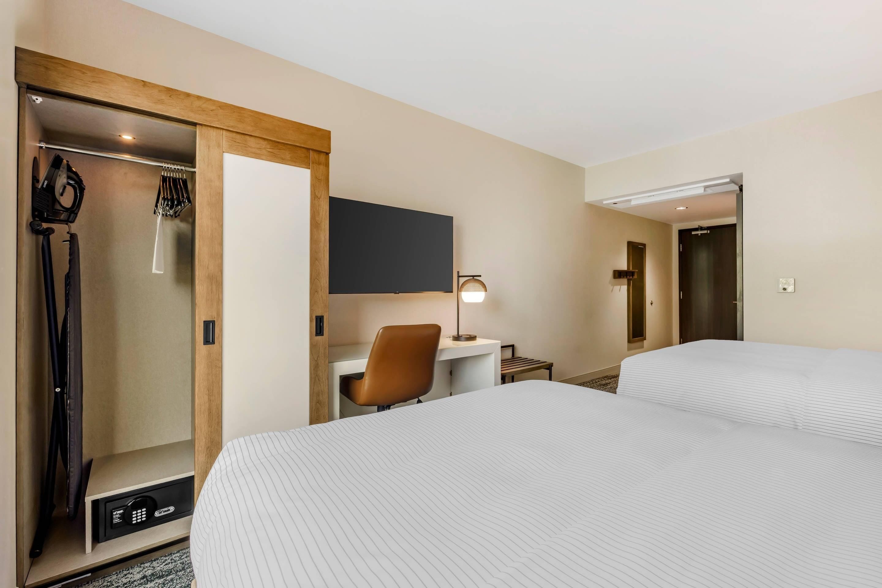 A hotel room with a bed, a desk with a chair, a TV mounted on the wall, and a shower area.