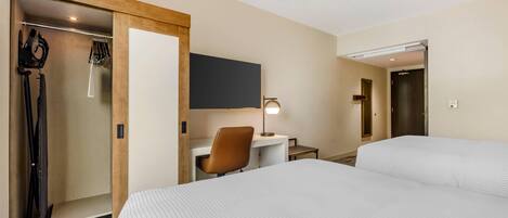 A hotel room with a bed, a desk with a chair, a TV mounted on the wall, and a shower area.