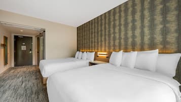 Quarto de hotel com duas camas, piso coberto por carpete, cabeceira de madeira com papel de parede estampado e mesa de cabeceira com abajur.