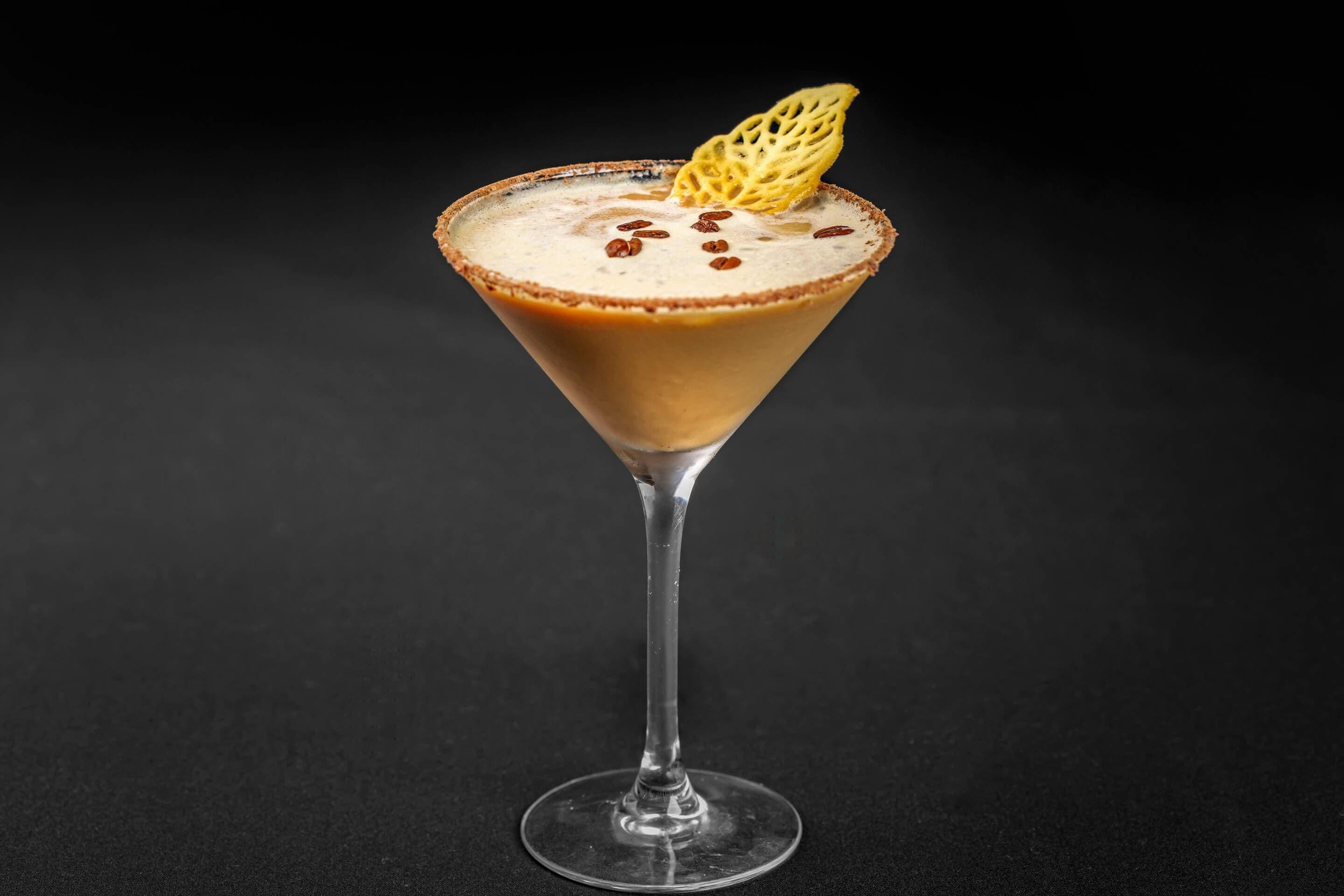 A martini glass with a caramel-colored rim, a frothy top, and a decorative sugar piece on a dark background.