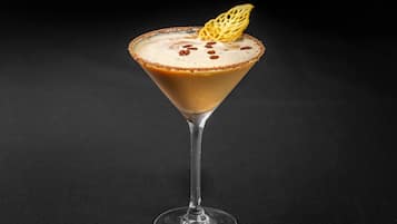 A martini glass with a caramel-colored rim, a frothy top, and a decorative sugar piece on a dark background.
