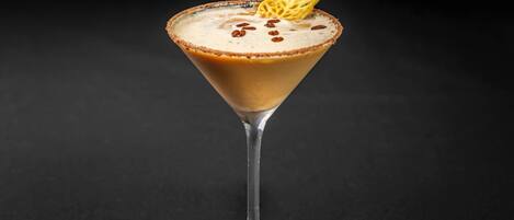 A martini glass with a caramel-colored rim, a frothy top, and a decorative sugar piece on a dark background.