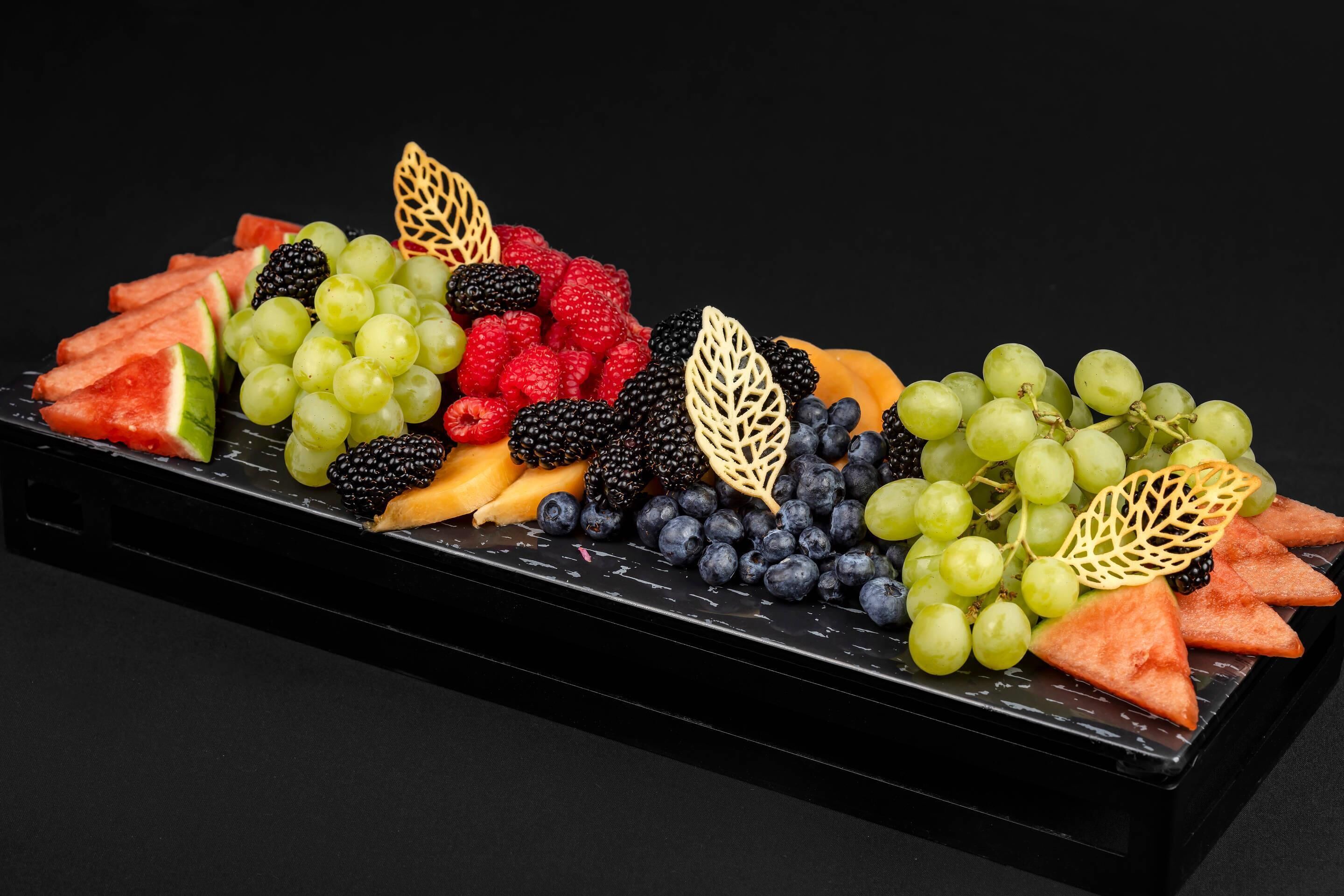 Une assiette de fruits comprenant de la pastèque, des raisins, des mûres, des framboises et des myrtilles.