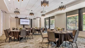 Un salón de conferencias con varias mesas, sillas y una pantalla de proyector mostrando 'CAMBRIA Portland - Pearl District'.