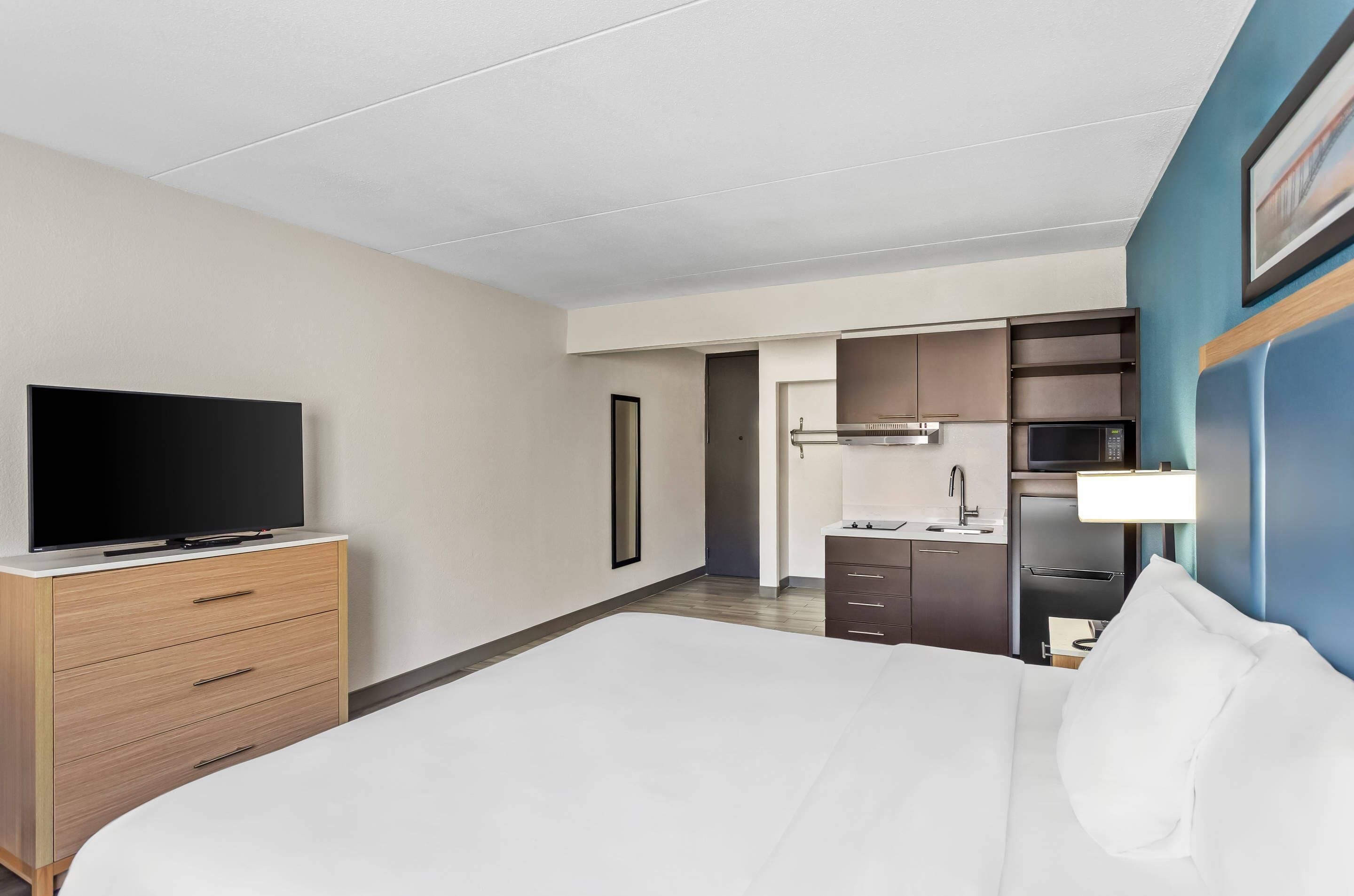 Una habitación de hotel con cama, televisor en una cómoda de madera, kitchenette y baño.