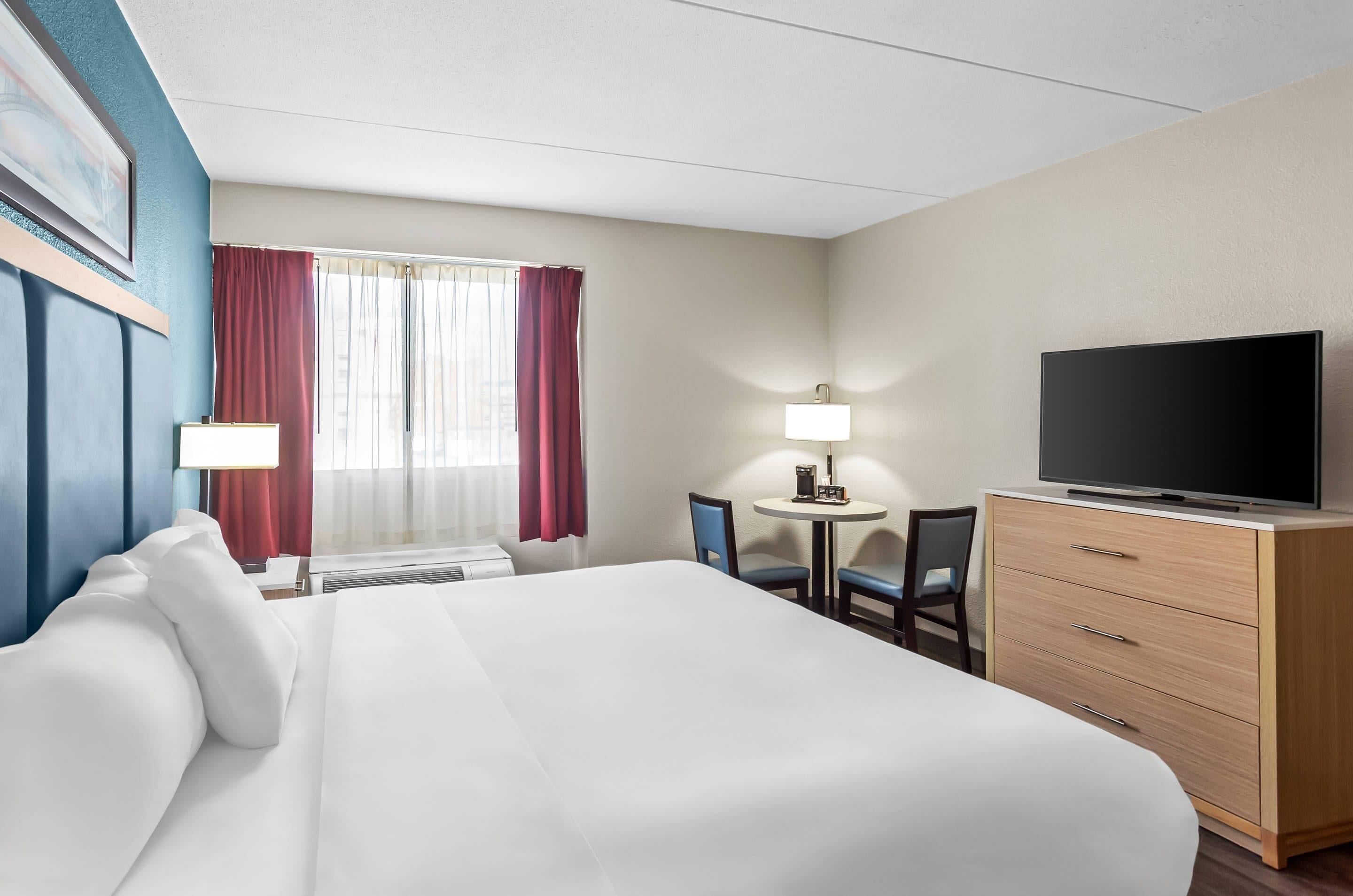 A hotel room with a large bed, a desk with a chair, a television, and a window with curtains.