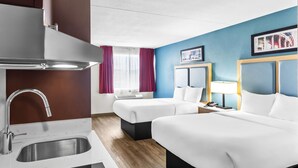 Quarto de hotel com cozinha compacta, duas camas, janela com cortinas e parede com detalhe azul.