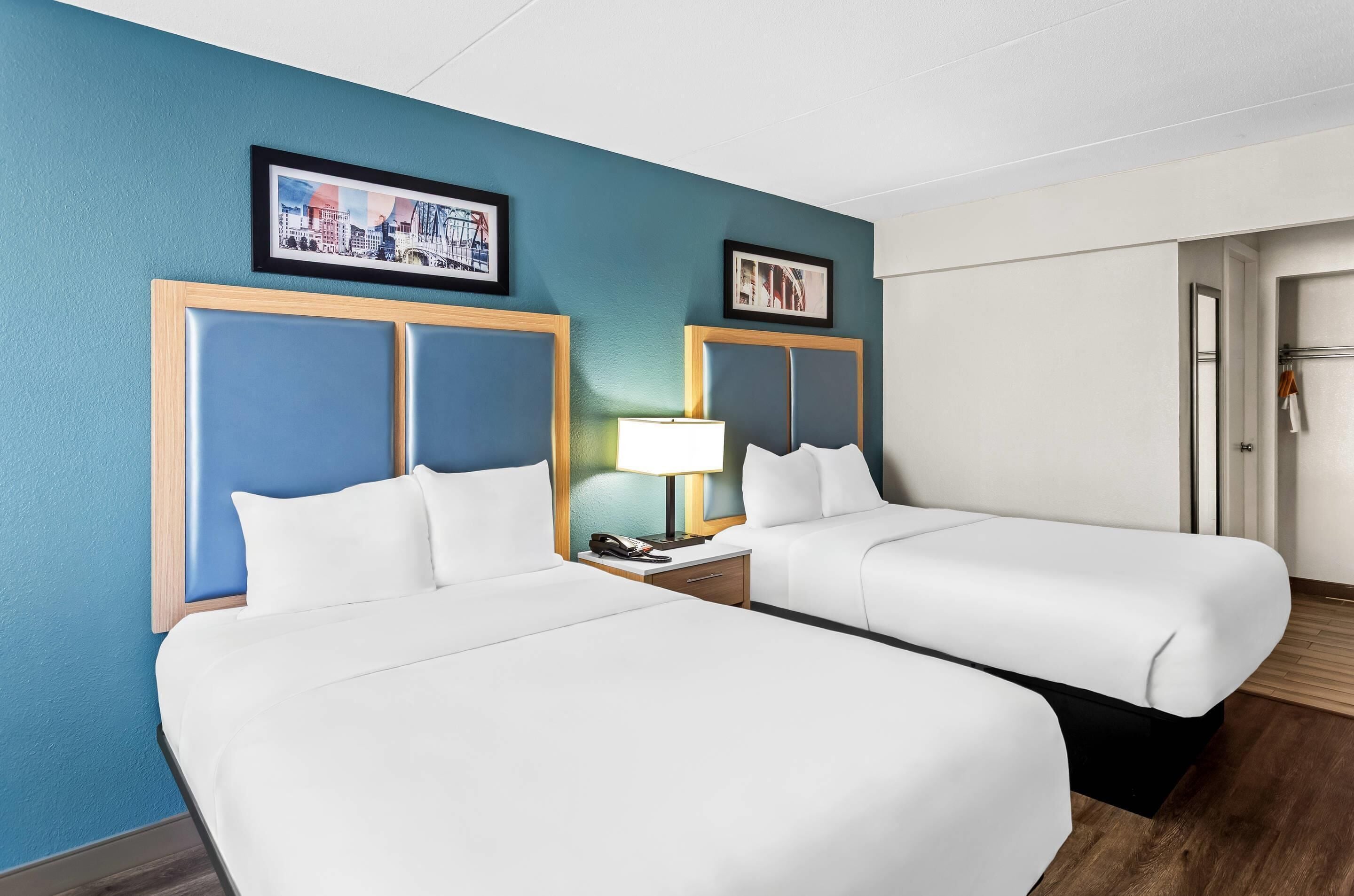 Een hotelkamer met twee bedden, een nachtkastje met een lamp en ingekaderde foto's aan de muur.