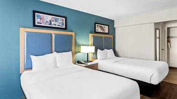 Een hotelkamer met twee bedden, een nachtkastje met een lamp en ingekaderde foto's aan de muur.