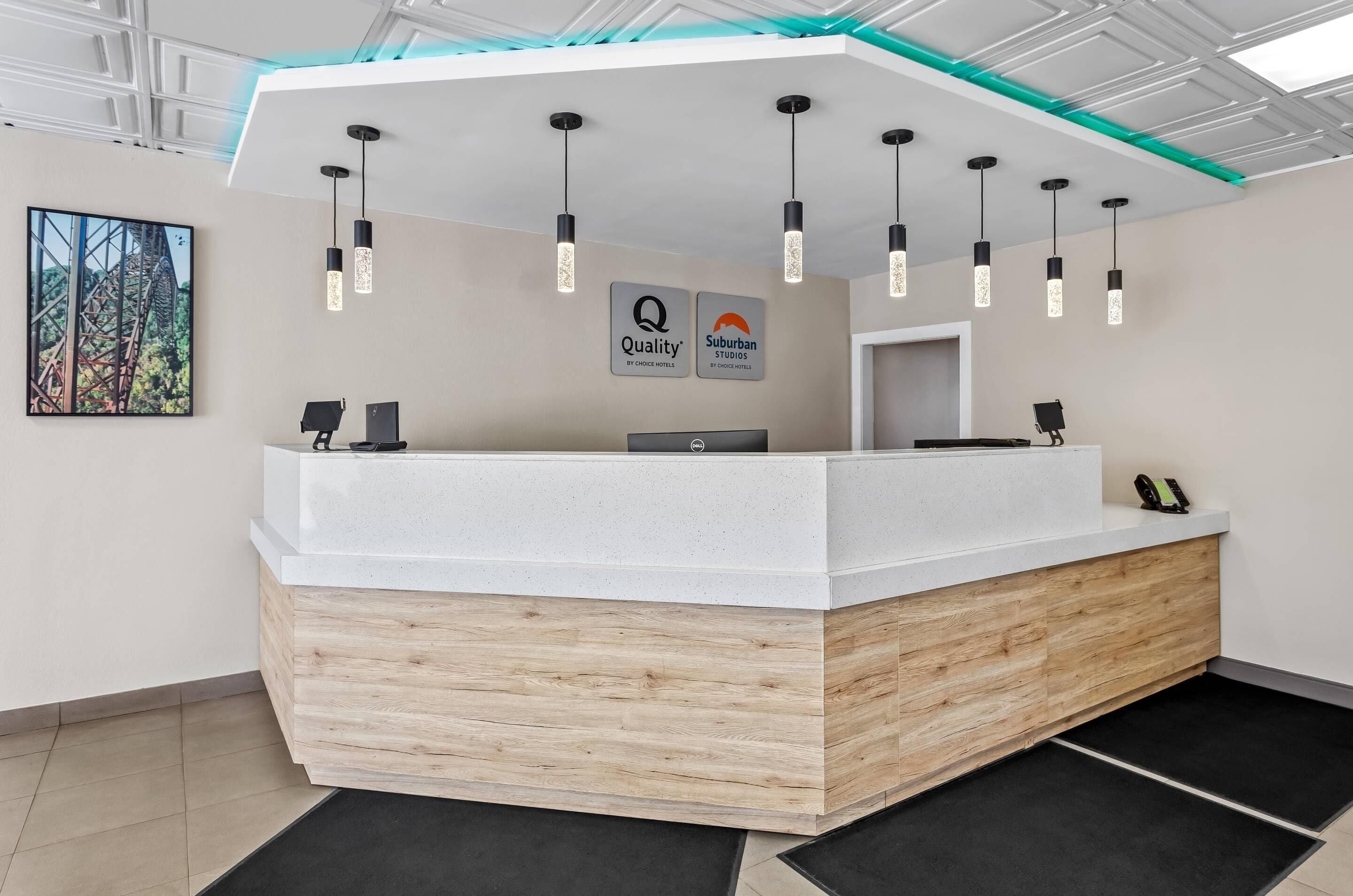 Un mostrador de recepción con encimera blanca, base de madera y lámparas colgantes. Encima del mostrador hay dos letreros: uno con la palabra 'Quality' y otro con 'Suburban Studios'.