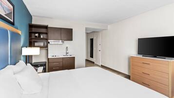 Habitación de hotel con cama, televisión, escritorio con lámpara, microondas y kitchenette pequeña.