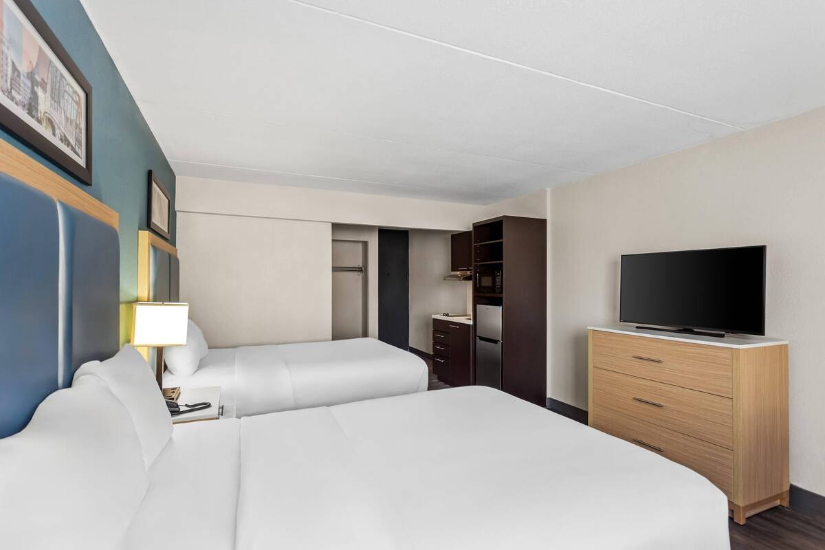 A hotel room with two beds, a TV, a dresser, and a desk with a lamp.