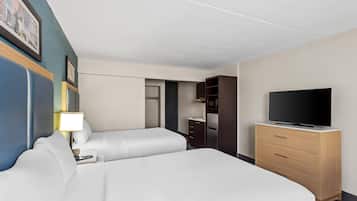 A hotel room with two beds, a TV, a dresser, and a desk with a lamp.