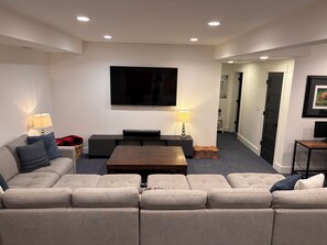 A modern living room with a large flat-screen TV, a sofa, a coffee table, and two lamps.