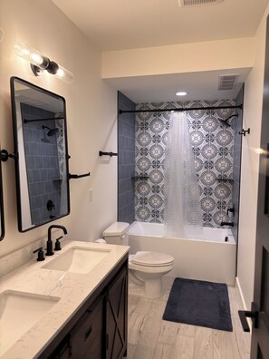 A modern bathroom with a large mirror, a sink, a toilet, and a bathtub.