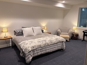 A bedroom with a bed, two bedside tables, a chair, a lamp, and a window.