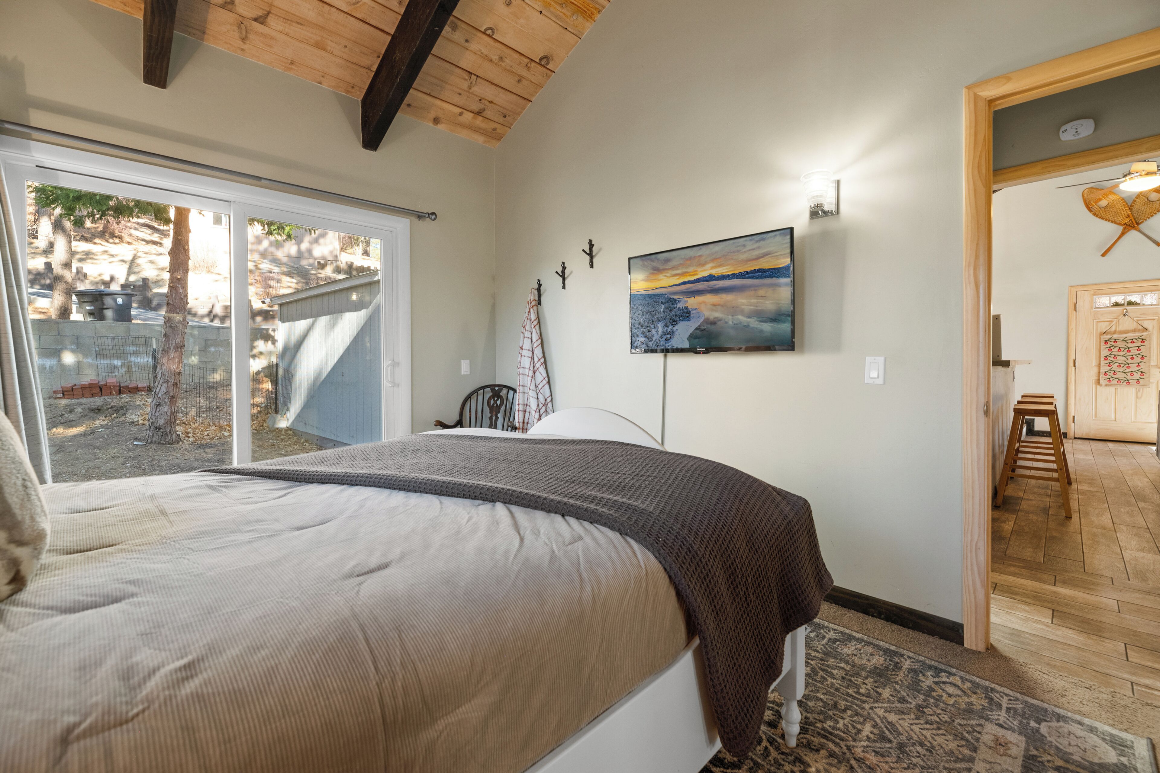 Une chambre avec un grand lit, une porte-fenêtre coulissante donnant sur un jardin, un tableau accroché au mur et un plafond en bois.