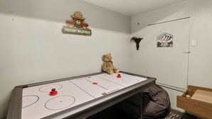 Una habitación con una mesa de juego tipo bolos, un oso de peluche y un cartel en la pared que dice "PREVENT WILDFIRES!".