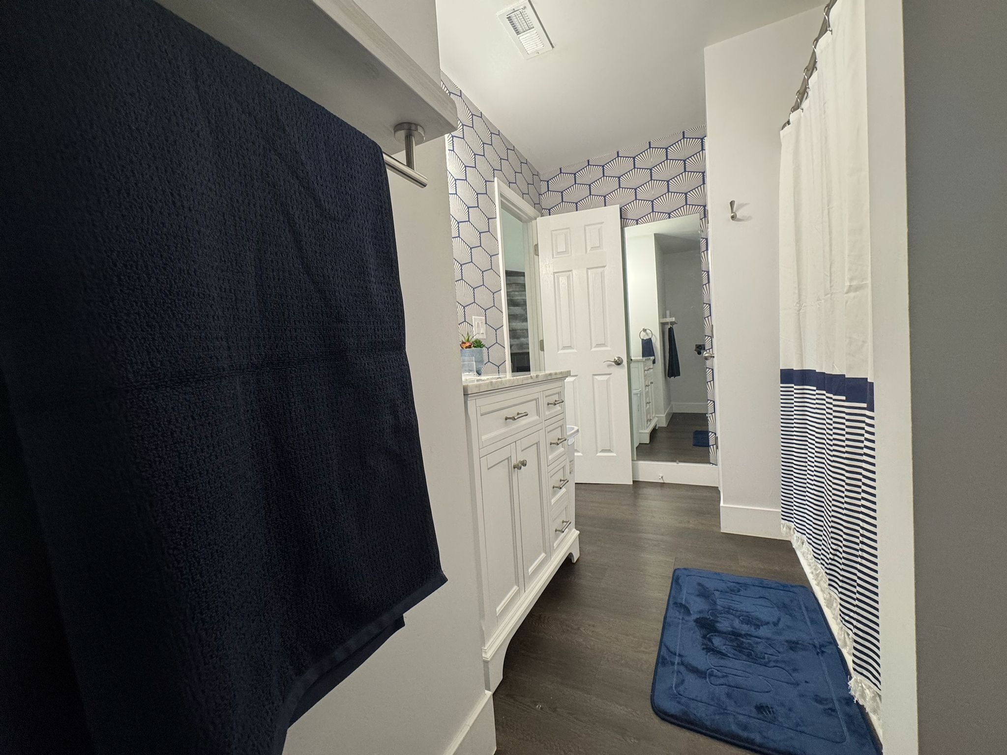 A hallway with a dark blue towel hanging on a rack, white cabinets, a blue bath mat, and a patterned wall.