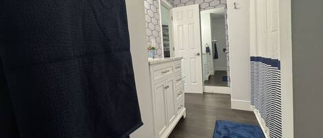 A hallway with a dark blue towel hanging on a rack, white cabinets, a blue bath mat, and a patterned wall.