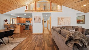 Un vaste espace de vie aménagé dans un style industriel, avec un plafond en bois, une mezzanine, une cuisine et un coin repas.