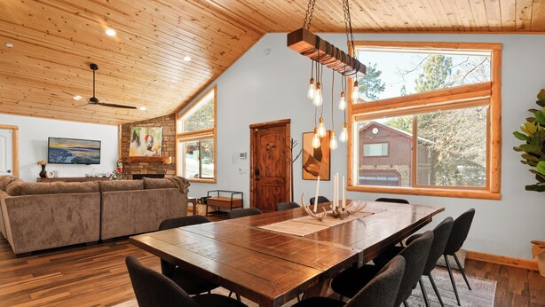 Un vaste espace de vie comprenant une table à manger en bois, des sièges confortables et de grandes fenêtres offrant une vue sur l’extérieur.