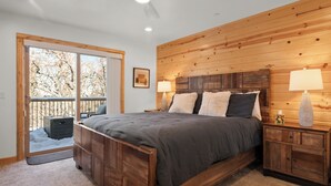 Une chambre à coucher avec une tête de lit en bois, un grand lit, une table de chevet avec une lampe, et une vue sur un espace extérieur enneigé, visible à travers une porte coulissante.