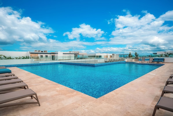A rooftop pool with clear blue water, surrounded by lounge chairs and a glass railing.