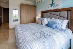 A bedroom with a large bed, a wooden wardrobe, a mirror, and a wall-mounted air conditioner.