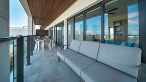 A balcony with a wooden ceiling, a white sofa, and a dining area with chairs and a table. - 2 BR Condo - Rooftop Pool At Ipanema 504 (Playa del Carmen)