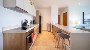 A modern kitchen with wooden cabinets, a built-in oven, a refrigerator, and a coffee maker. There are two bar stools and a small island with a sink. - 2 BR Condo - Rooftop Pool At Ipanema 504 (Playa del Carmen)