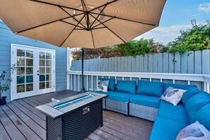 Eine Terrasse im Freien mit einem beigefarbenen Sonnenschirm, einem Tisch mit Glasplatte und einem blauen Sofa mit Kissen.