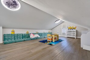 Amplia habitación en ático con techo alto, sofá color turquesa, mesa de juegos de madera y cómoda blanca.