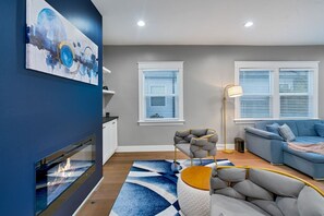 Ein modernes Wohnzimmer mit Kamin, einem blauen abstrakten Gemälde, einem grauen Sofa und einem blauen Couchengel.