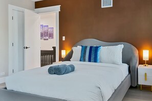 Une chambre d’hôtel moderne avec un grand lit, une table de chevet avec une lampe et une vue sur la ville par une porte ouverte.