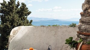 Un balcon avec une table et des chaises, offrant une vue panoramique sur la mer et les montagnes.