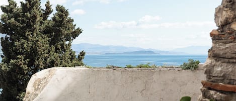 A balcony with a table and chairs, overlooking a scenic view of the sea and mountains.