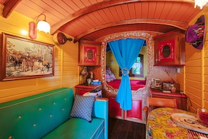 A cozy room with a green sofa, a wooden bench, a table with a floral tablecloth, and a bed with a blue canopy. - Petite maison 'Roulotte La Casetta Rita' with Shared Pool, Private Terrace & Shared Garden (Chambon)