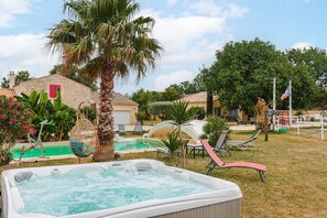 Un jacuzzi, mobiliario de exterior y una piscina en un jardín.