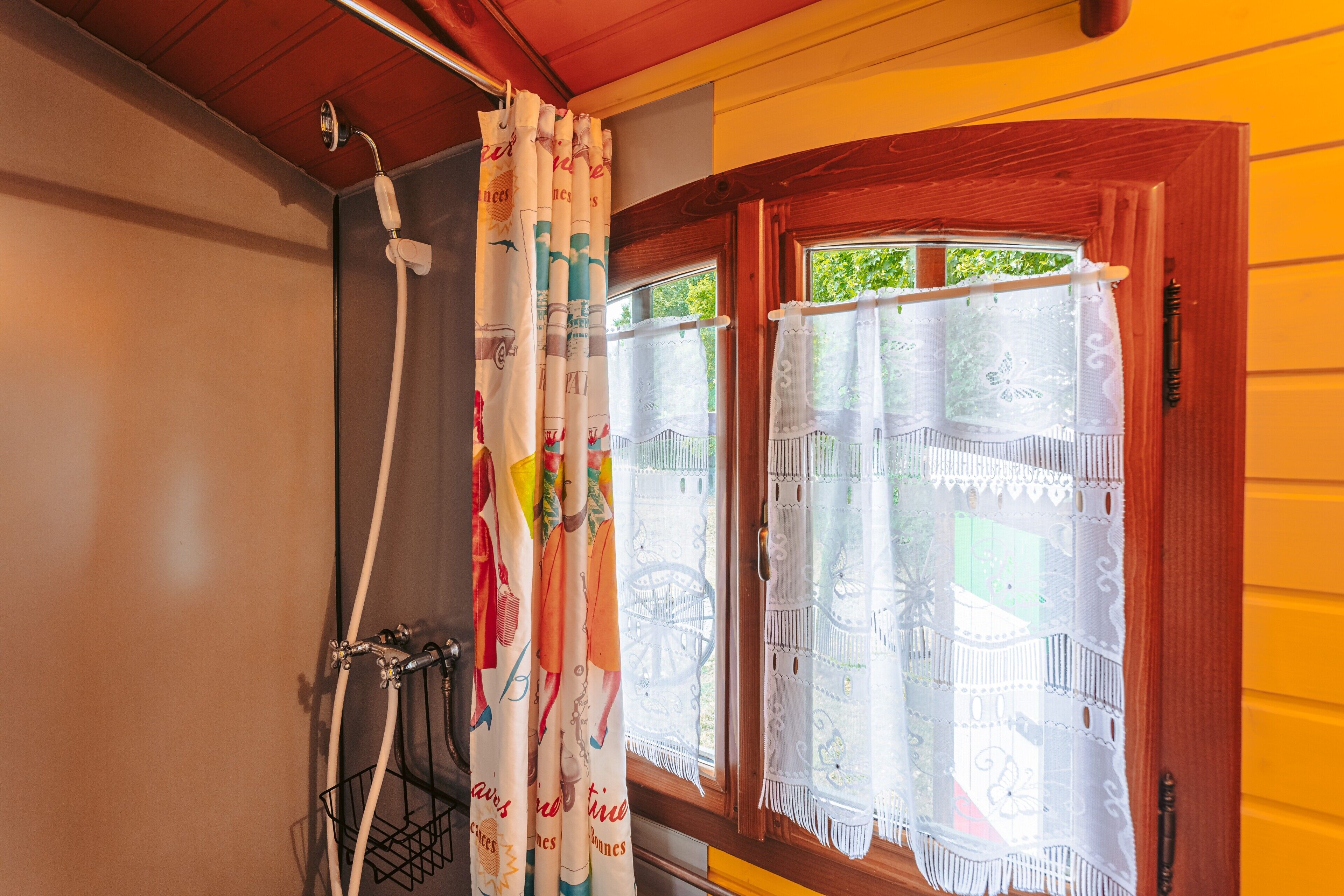 Une salle de bain avec une douche, une fenêtre avec un rideau et une porte en bois.