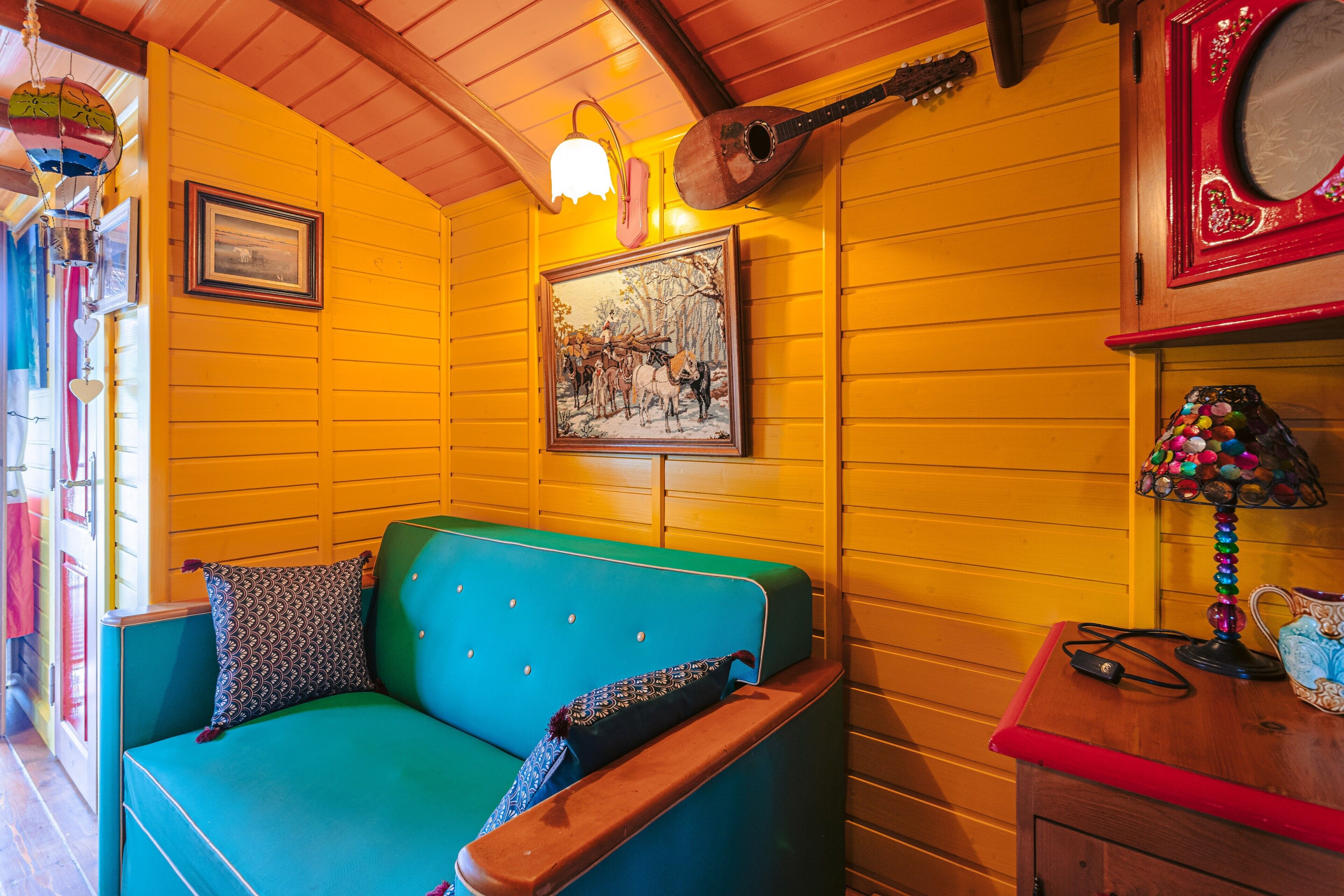 A room with a teal sofa, a guitar, a framed painting, and a lamp.