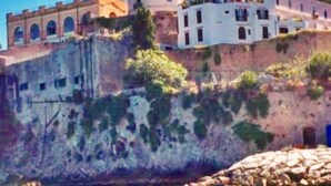 Un edificio frente al mar con varios niveles, con ventanas de arco y una mezcla de estilos arquitectónicos.