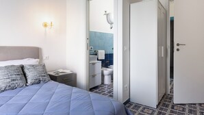 Habitación de hotel con cama, mesita de noche, baño visible a través de una puerta abierta y armario.