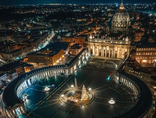 A nighttime view of St. Peter's Square with the Vatican's dome and the obelisk in the center.