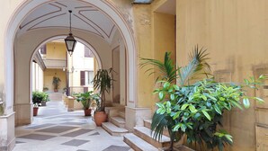 Un couloir au sol carrelé, agrémenté de plantes en pot et doté d’un escalier menant à un étage supérieur.